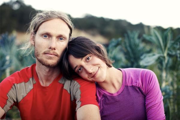 a young couple sitting in a field, the woman resting her head on his shoulder